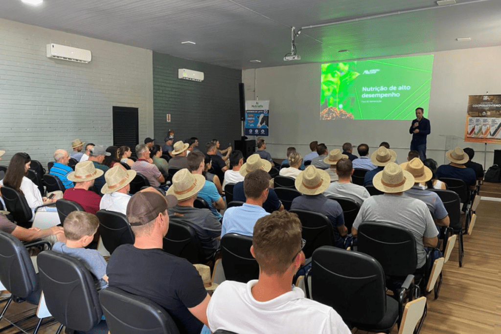 Foto de auditório com dezenas de cadeiras ocupadas, um palestrante na frente e imagens no telão ao fundo.