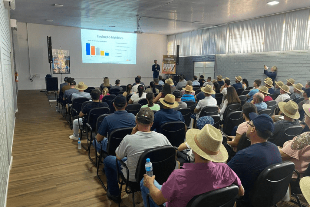 Foto de auditório com dezenas de cadeiras ocupadas, um palestrante na frente e imagens no telão ao fundo.
