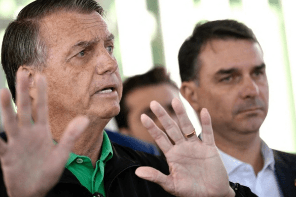 Jair Bolsonaro com o filho Flávio ao fundo após deixar hospital e seguir para prisão domiciliar.