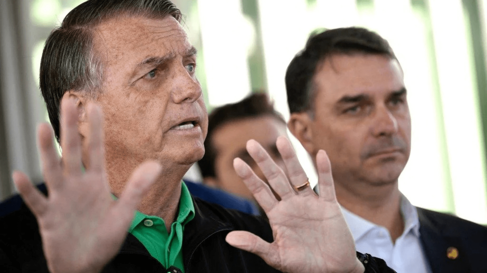 Jair Bolsonaro com o filho Flávio ao fundo após deixar hospital e seguir para prisão domiciliar.