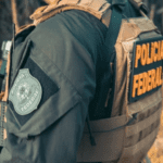 Imagem de um agente da Polícia Federal com colete e arma de costas e sem mostrar o rosto