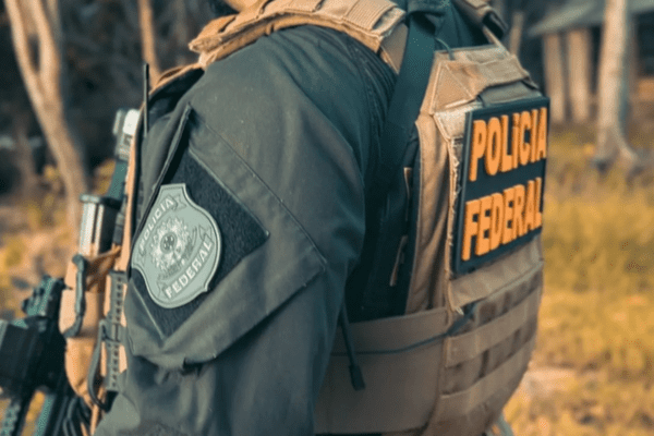 Imagem de um agente da Polícia Federal com colete e arma de costas e sem mostrar o rosto
