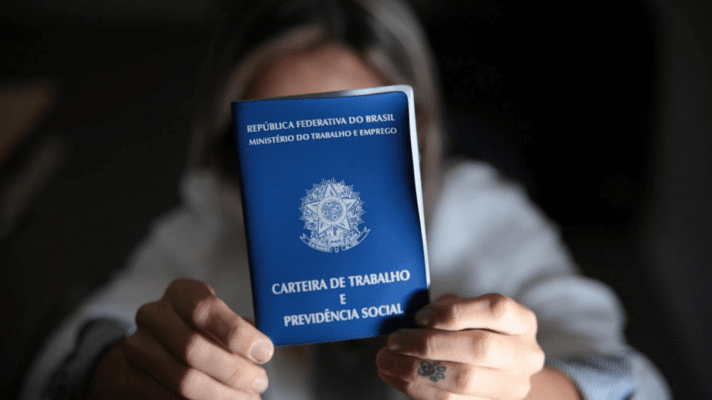 Imagem de pessoa desfocada segurando na frente do rosto uma Carteira de Trabalho