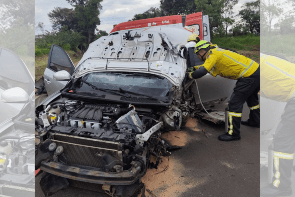 Imagem de carro com a frente destruída em acidente e bombeiro olhando pela janela.