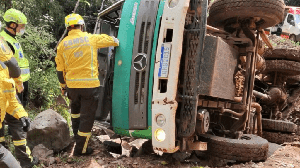 Imagem caminhão tombado com dois bombeiros ao redor