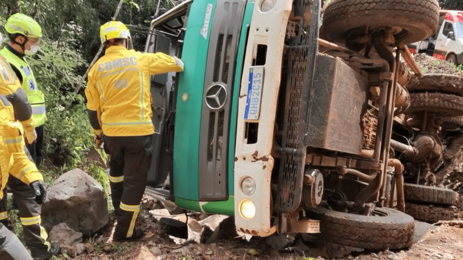 Imagem caminhão tombado com dois bombeiros ao redor