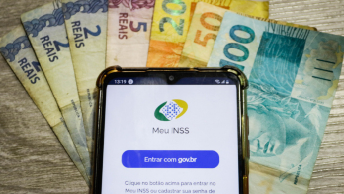 Celular com o aplicativo do Meu INSS aberto e notas de dinheiro por baixo