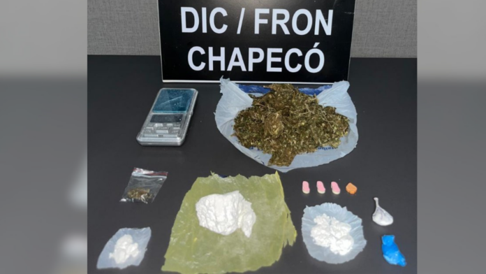 Placa do DIC/FRON Chapecó e na frente várias substâncias entorpecentes apreendidas em operação.