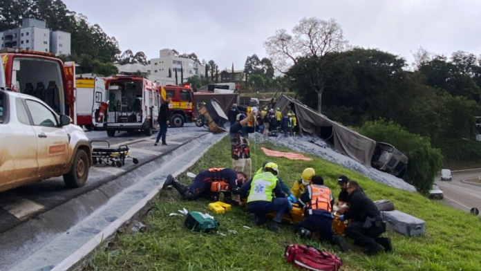 Caminhão tombado ao fundo na BR-282 em Cordilheira Alta e Bombeiros socorrendo vítima á frente.