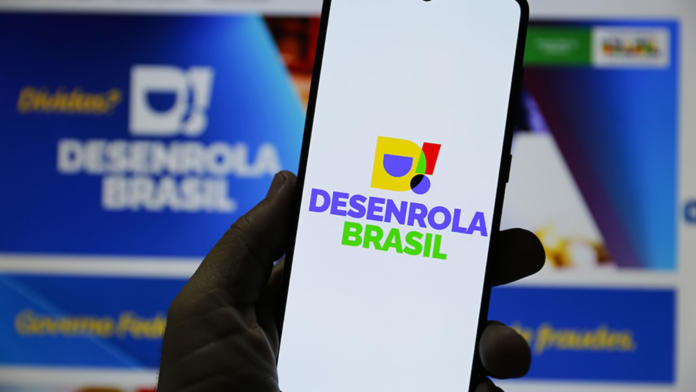Mão segurando celular com nome do pragrama do governo Desenrola Brasil na tela