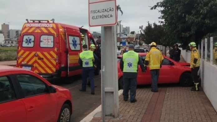 Veículo Gol vermelho batido em um muro e ambulância dos Bombeiros atrás com equipes ao redor.