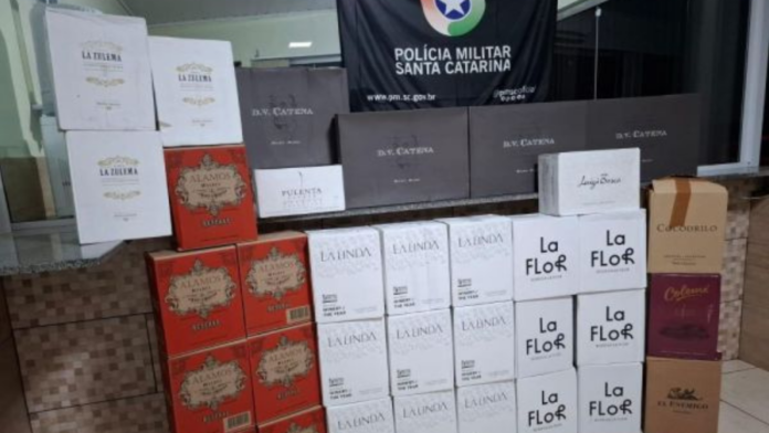 Dezenas de caixas variadas de vinho argentino e sobre a bandeira da Polícia Militar