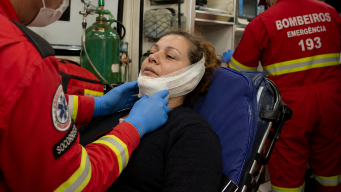 Imagem de IA mostra um bombeiro atendendo uma mulher com curativos no queixo e outro bombeiro atrás, dentro da ambulância
