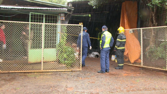 Bombeiros em frente á uma casa com portão de grade semi aberto amarelo.
