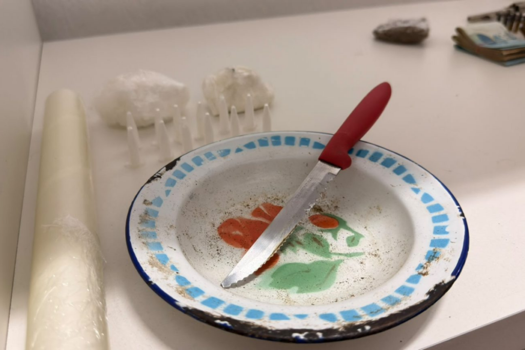 Prato com faca de cabo vermelho e ao lado pinos cheios de cocaína pronta para venda e uma pedra de cocaína.